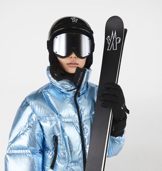 Woman in metallic skiwear jacket with mask and skis