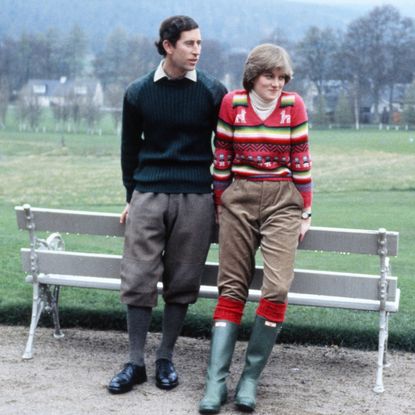 Prince Charles and Princess Diana leaning on a bench wearing boots