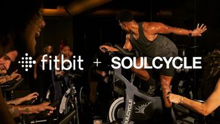 A promotional image of a SoulCycle class with the instructor wearing a Fitbit Charge 6, with the words "Fitbit + SoulCycle" transposed on top.