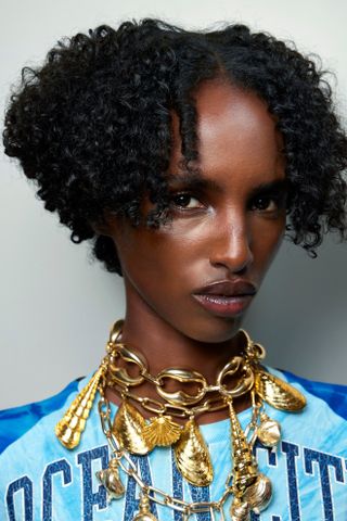 A model with a curly bob hairstyle draped in gold jewelry.