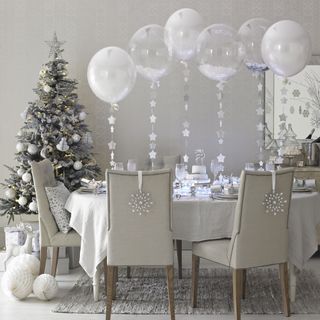 Grey dining room with table and chairs with Christmas decorations and balloons next to Christmas tree.