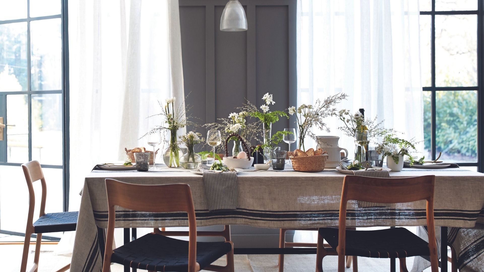 Grey and white dining room with retro chairs and table with tablecloth laid with spring flower displays