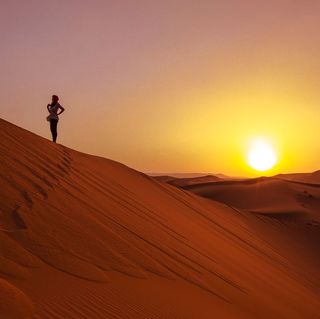 Women standing on a sand dune with sun setting