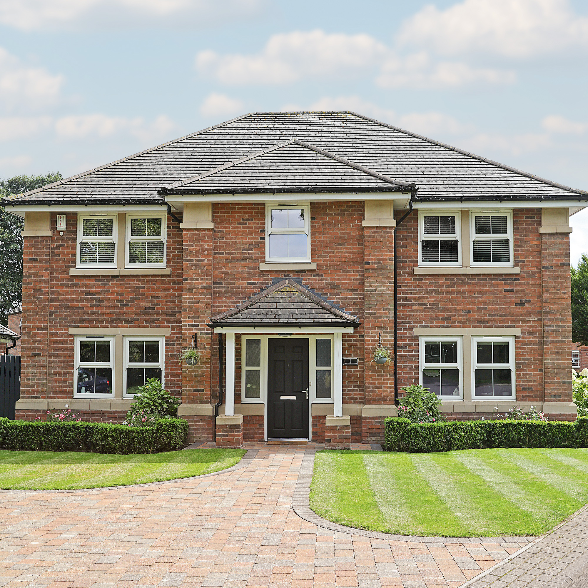 exterior of redbrick house with brick drive way and two small green lawns and a portico style porch