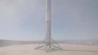 a scorched white rocket stands upright on a concrete landing pad