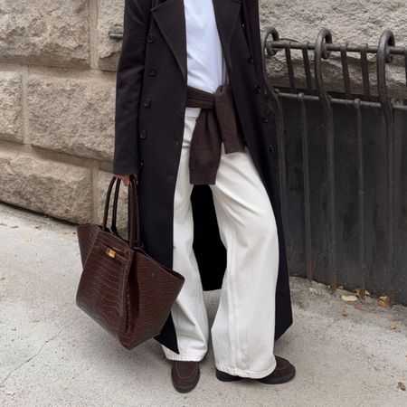 A content creator wears cream trousers with brown suede shearling-lined loafers and a brown bag