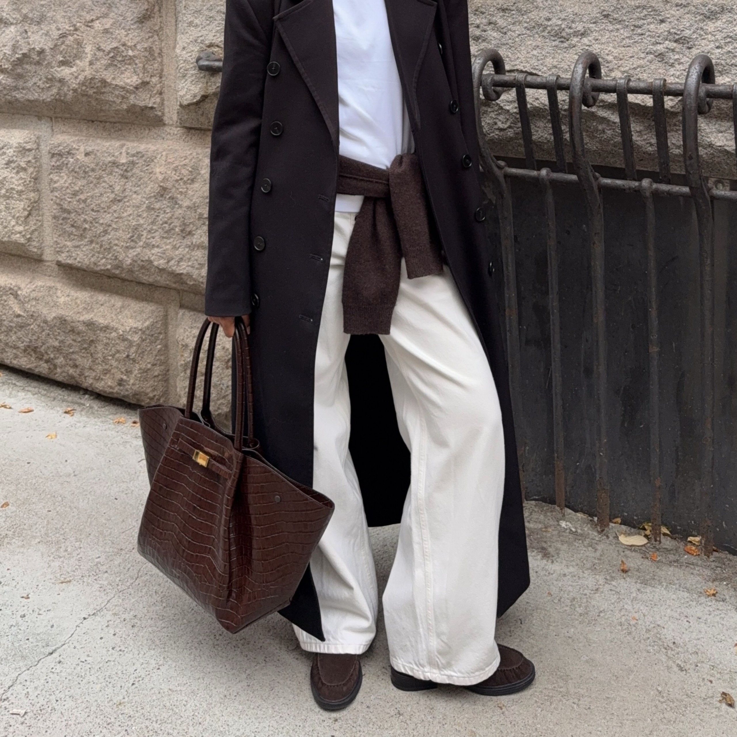 A content creator wears cream trousers with brown suede shearling-lined loafers and a brown bag