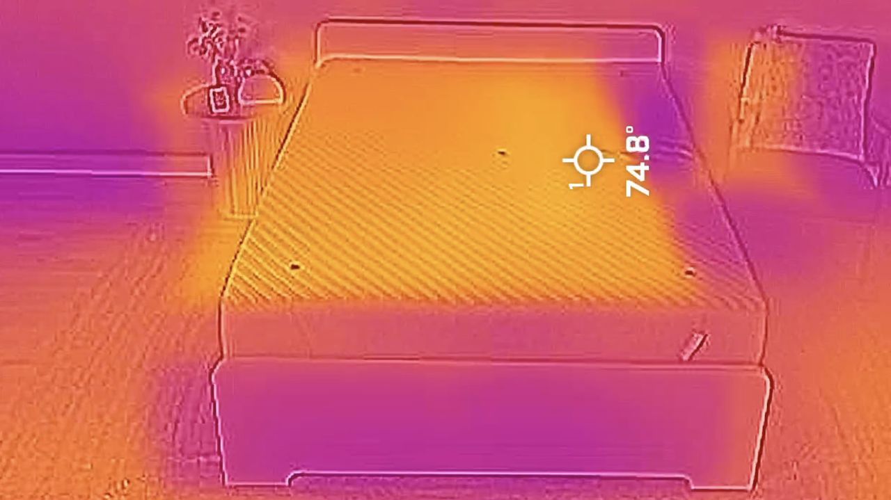 A picture of the Siena Memory Foam Mattress taken with a thermal imaging camera. This image is from after 15 minutes of heat dispersion &mdash; the yellow area stretching across the mattress (contrasted with the purple cooler patches around the room) indicates most of the warmth has left the mattress. However, you can see a faint imprint on the right side of the bed from where our tester, sleep writer Ruth Jones, was lying on the mattress. This shows that the Siena hasn't completely removed all the warmth it initially absorbed. A target displaying a temperature reading of 74.8&deg;F is palced over the hot spot.