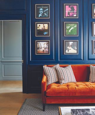 Living room with dark blue panelled walls, wooden flooring, grey rug and plush velour sofa and artwork on the wall