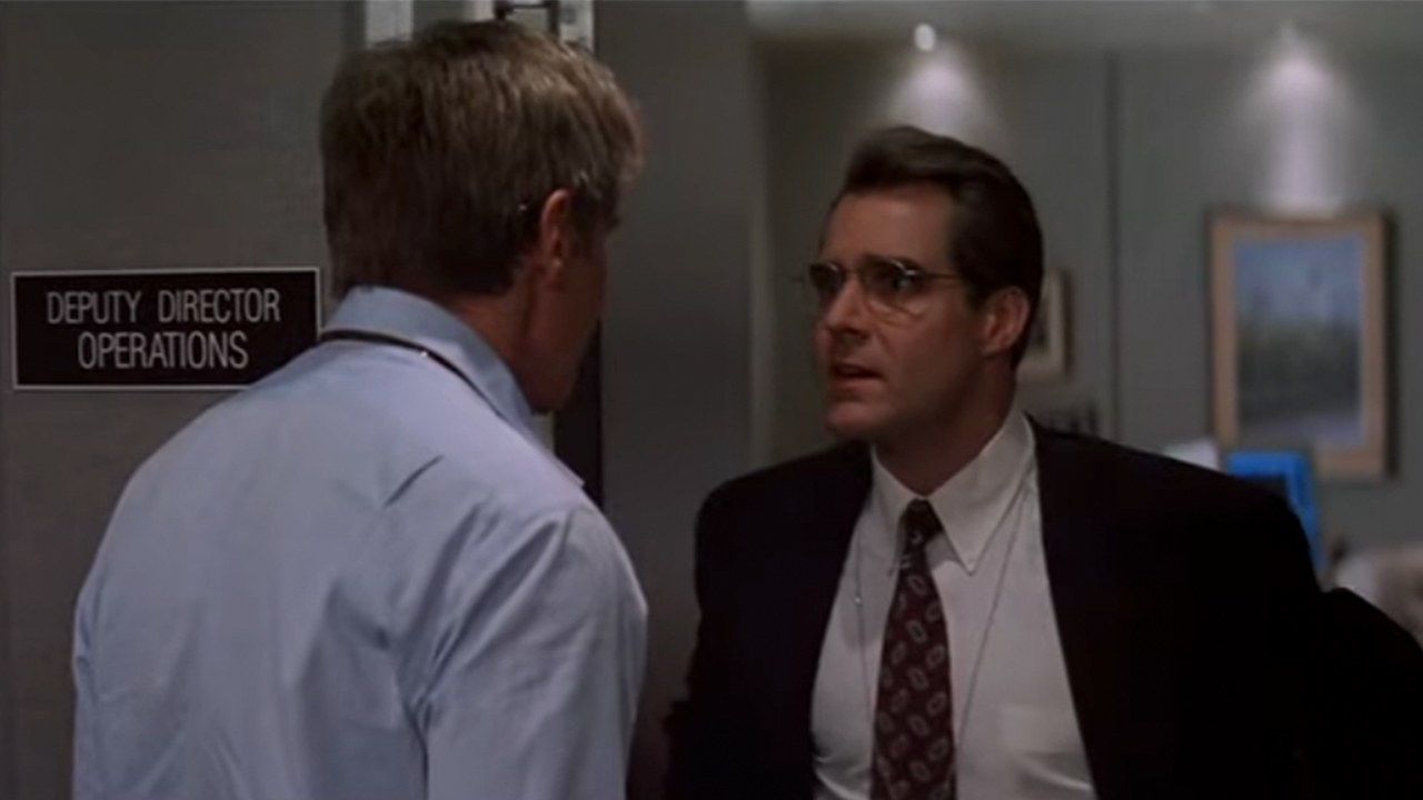 Henry Czerny in a suit, talking to Harrison Ford, whose back is to the camera.