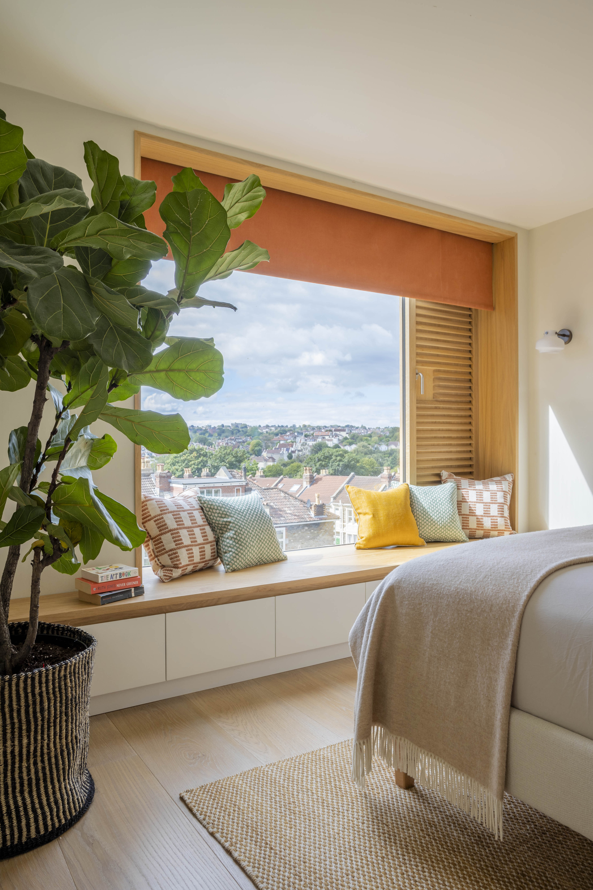 bedroom with window seat painted yellow and styled with cushions, timber flooring, and large fiddle leaf potted plant, and throw over the end of the bed