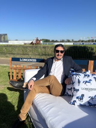 Fernando Gomez Dossena sitting on a white lounge chair next to a blue and white Longines pillow.