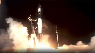 a black and white rocket lifts off above a plume of fire and smoke
