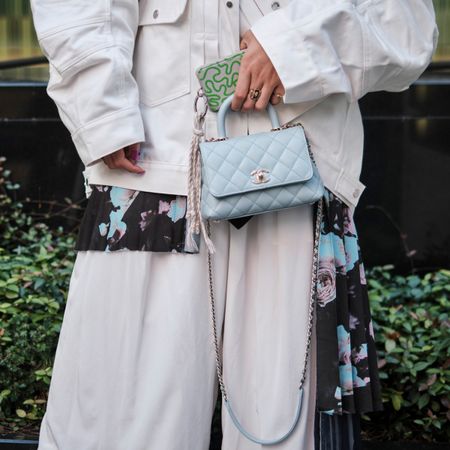 a close-up street style photo of a woman holding a crossbody cell phone bag with a white denim jacket