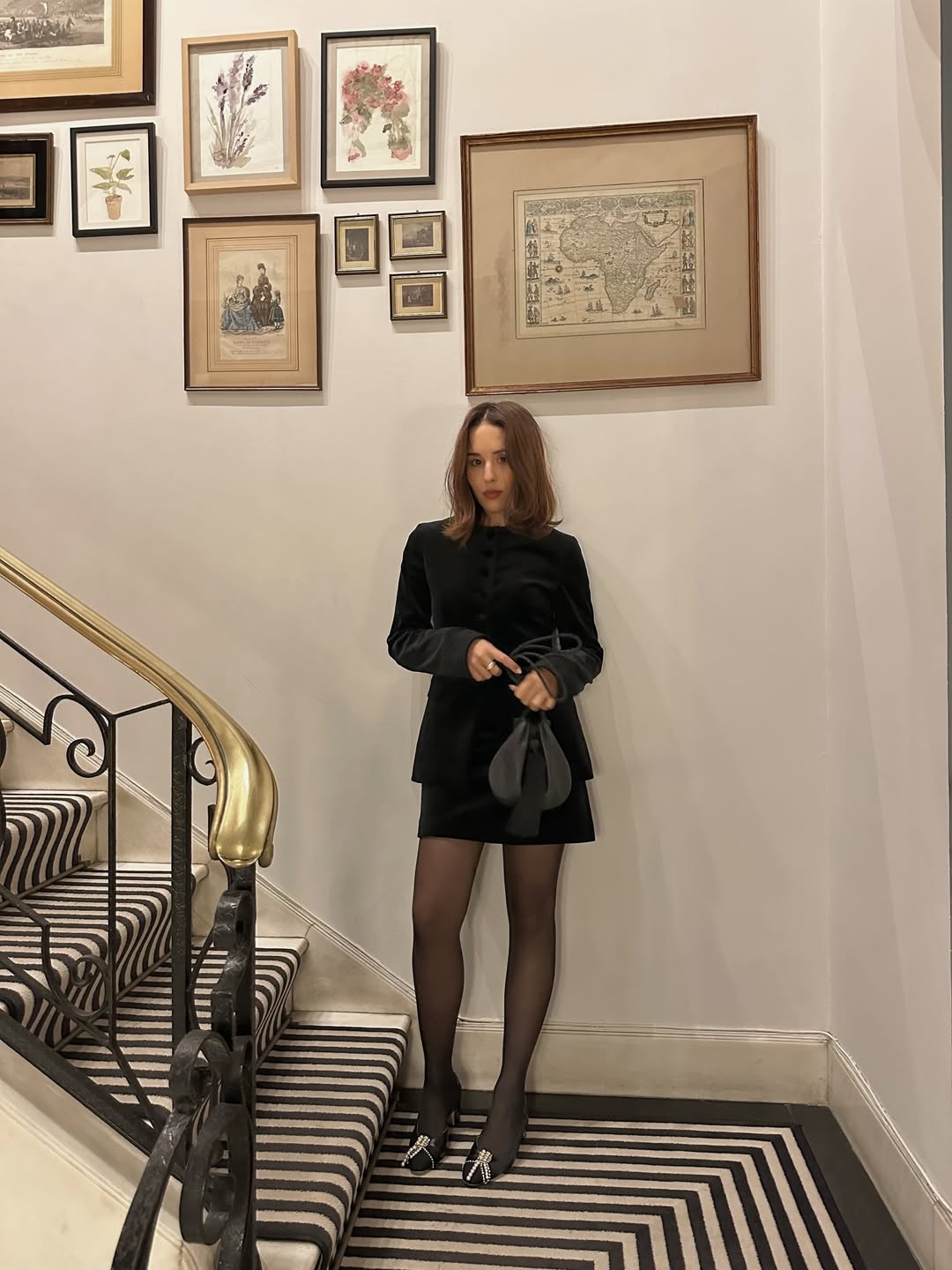 @deborabrosa wearing a black skirt, black jacket, tights, and low heels