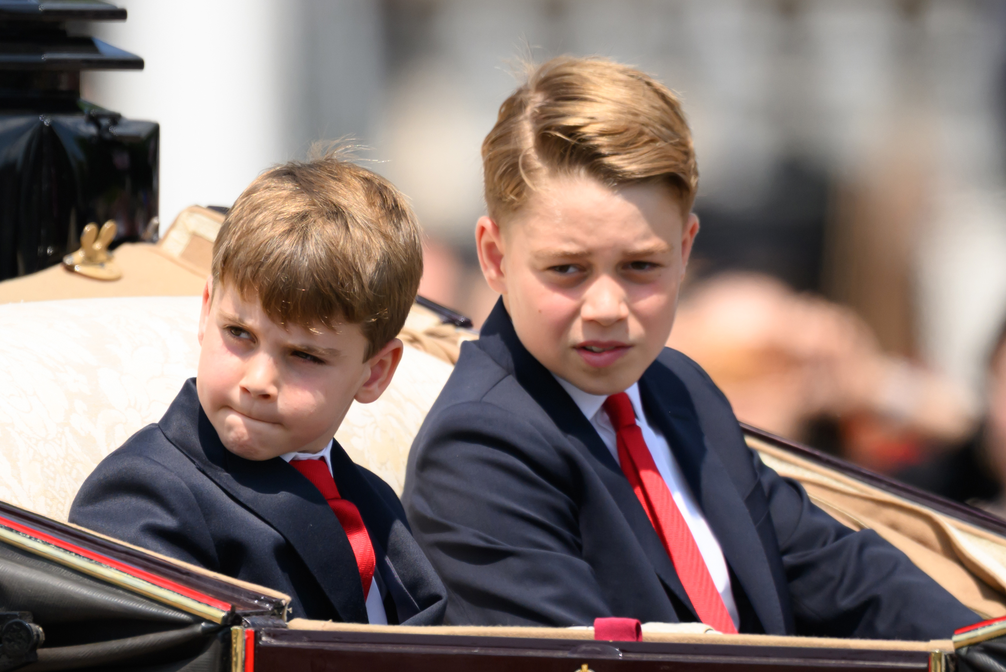 Prince George at Trooping the Colour 2025 wearing a navy suit with a white shirt and a red tie, and joining the Royal Family on the Buckingham Palace balcony