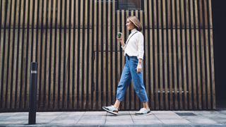 A woman walking along a sidewalk with a cup of coffee