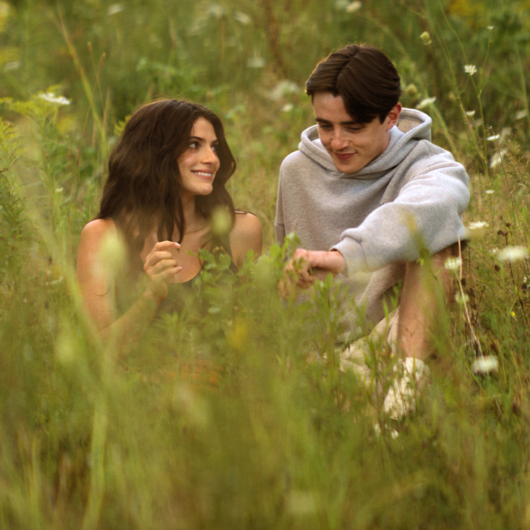 Two teenagers (Ella Rubin as Annie Jacobson and Daniel Quinn-Toye as Rory) sit in a field of grass and wildflowers, in the Prime Video series 'Sterling Point.'