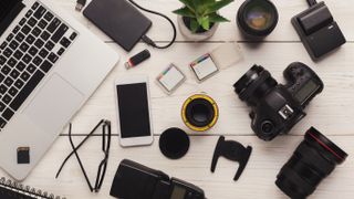 Different tech products like a laptop, camera, mobile phone and camera accessories on a table