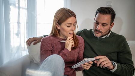 Couple on sofa at home planning together with documents, pen and focused, collaborative expressions