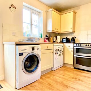 White kitchen with food floor, oven, washing machine, black kettle and toaster