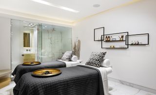 Two spa beds with black and white bedding. Two trays with hot stones are on the beds