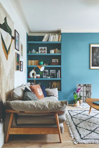 Lea-Wilson house: Living room with blue feature wall, alcove shelving, grey sofa and fabric wall hanging