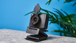 a black small 4K webcam with a red button photographed on a beige surface against a blue background