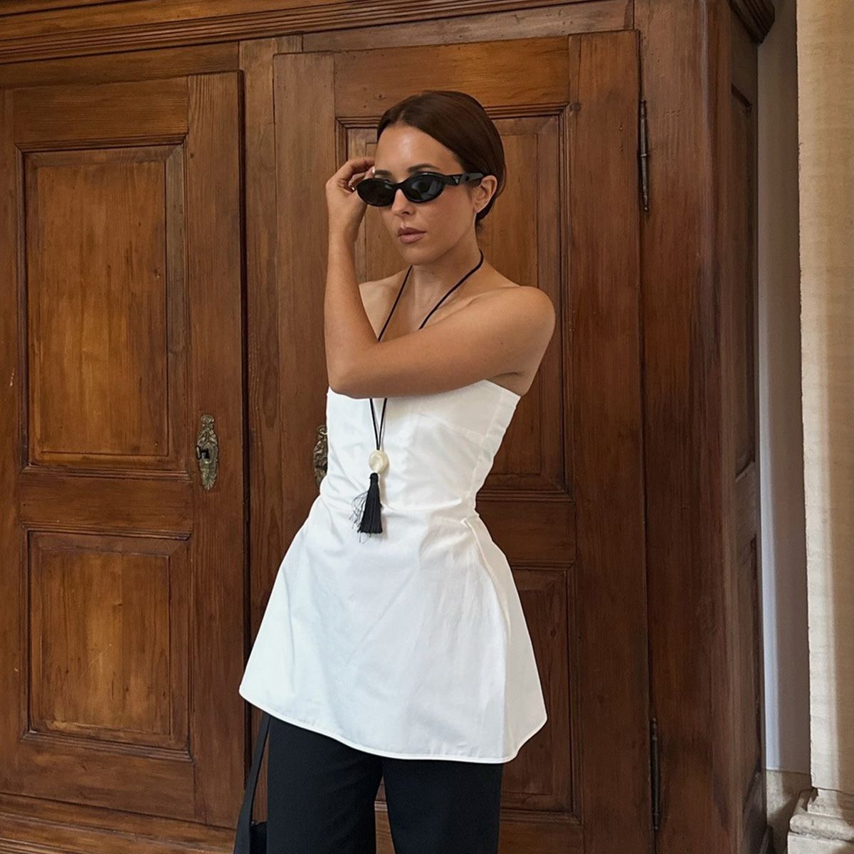 Deborah Rosa is wearing a white peplum top, black pants and a tassel pendant necklace.