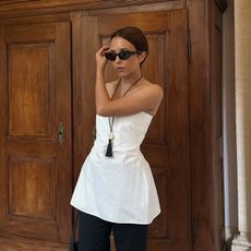 Debora Rosa wearing a white peplum top, black pants, and a tassel pendant necklace.