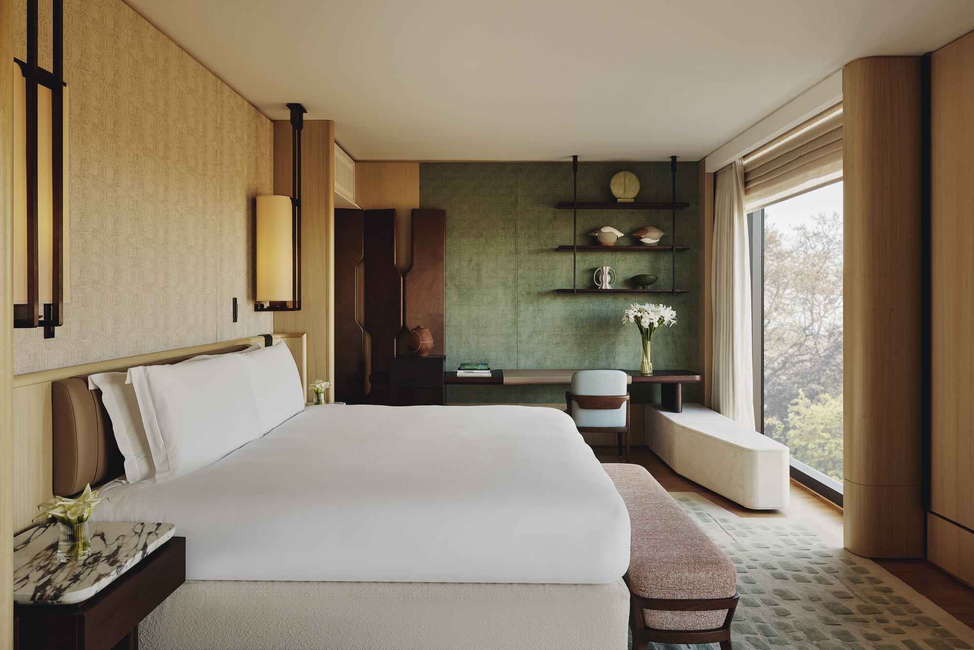Image of a bedroom inside the Emory hotel in London. The bed is pressed with white linens, and the room otherwise has a warm beige color palette with hints of pink and green.