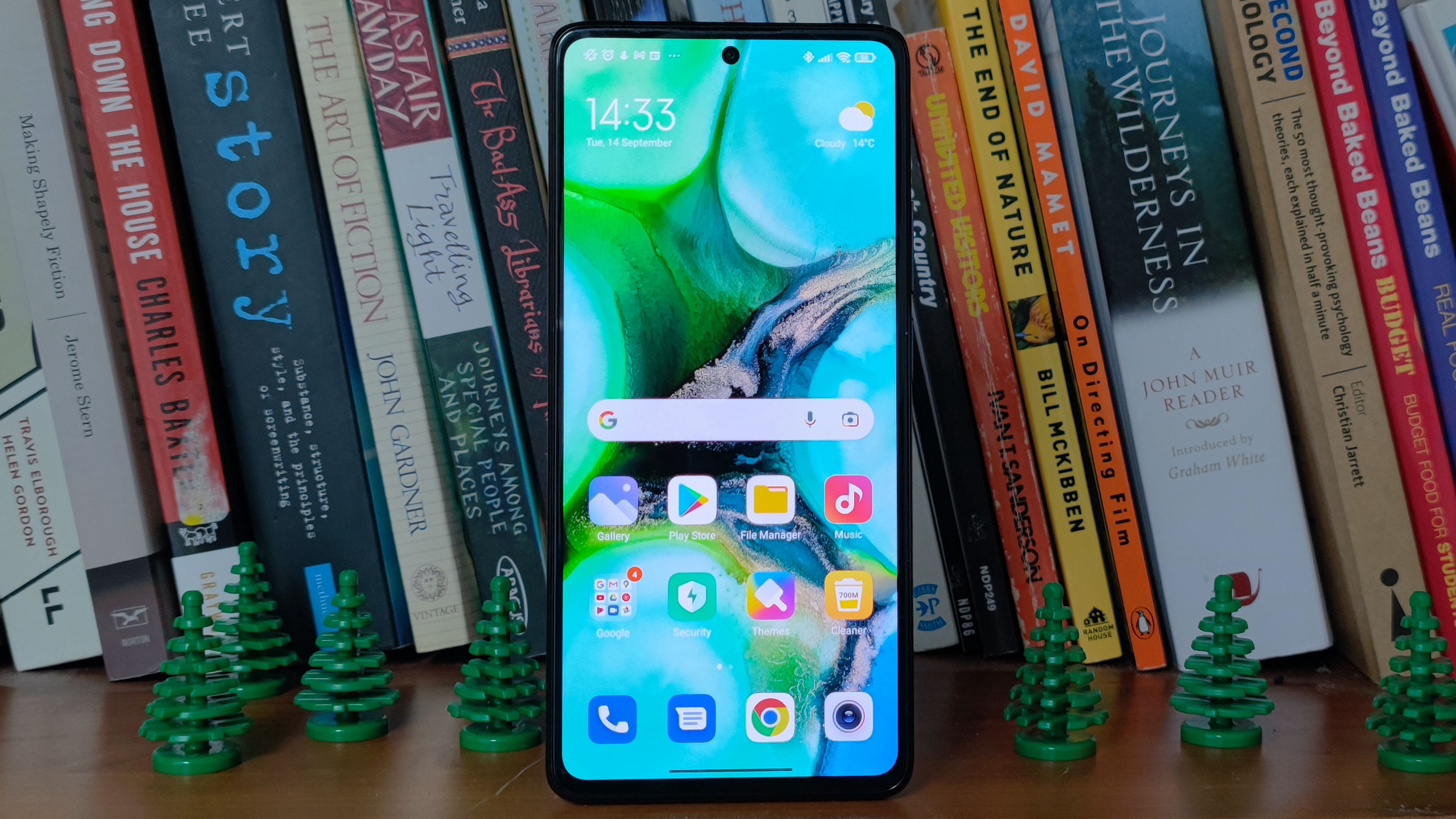 A Xiaomi 11T Pro in front of some books, flanked by plastic trees