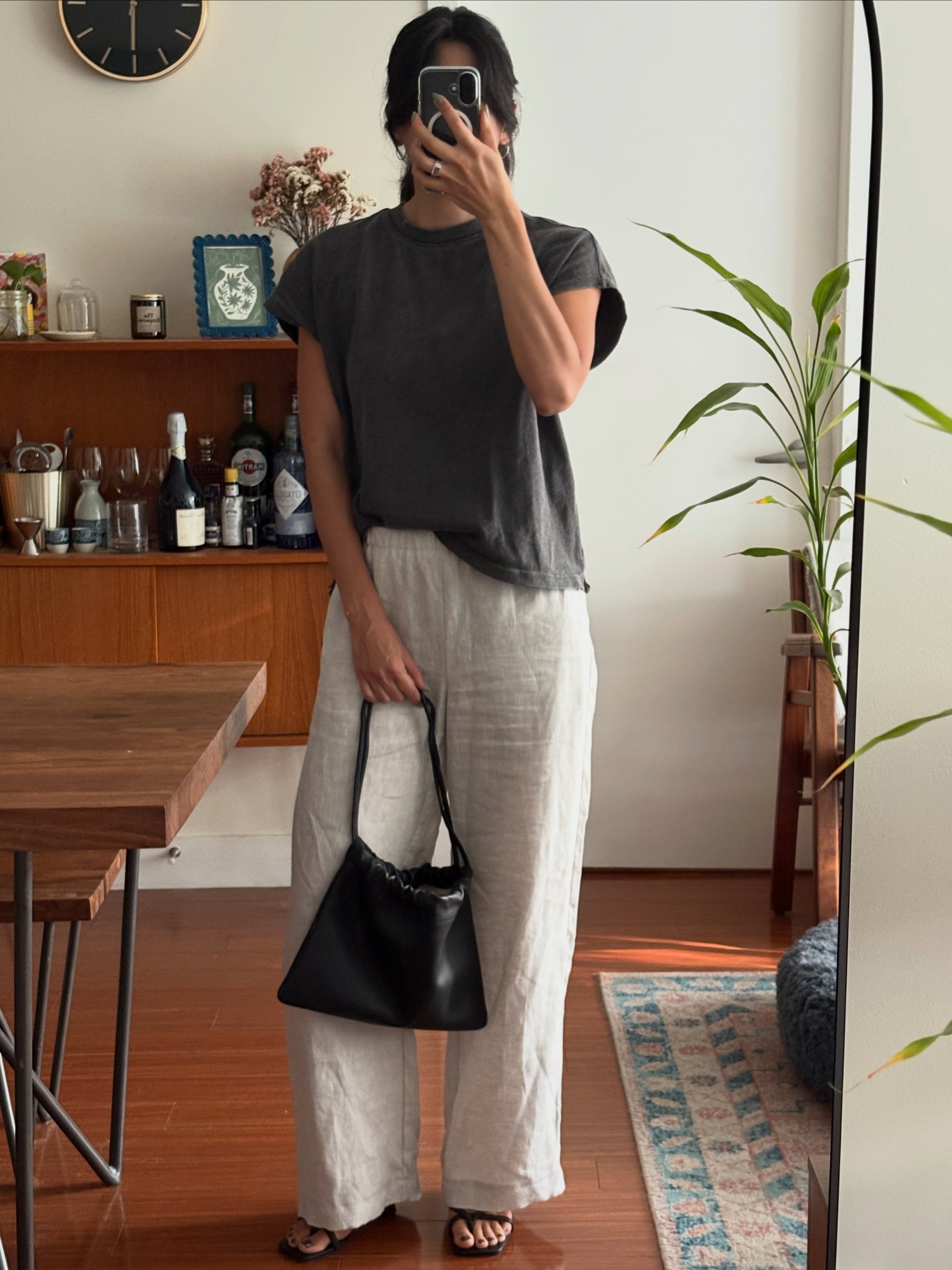 Woman wears grey tee, beige trousers and carries black drawstring bag from The Horse