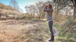 A woman on a trail looking through binoculars