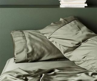 Corner of the ettitude Signature Sateen Sheet Set on a bed against a green wall.