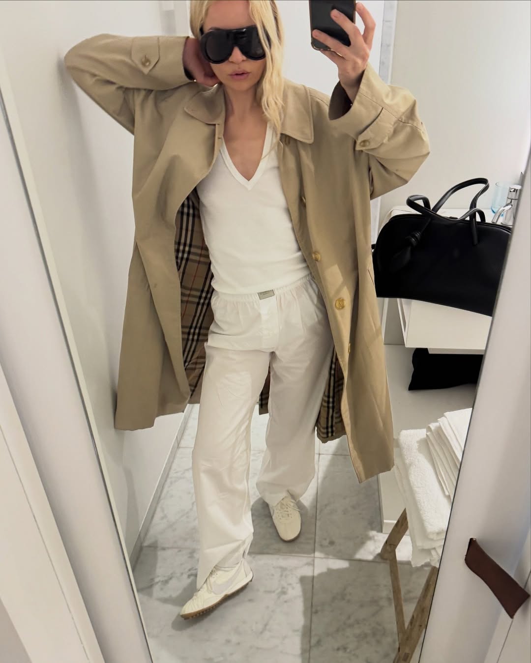 A woman wearing an all-white outfit with a trench coat and oversized sunglasses, part of the Spring Basics Outfit 2026.