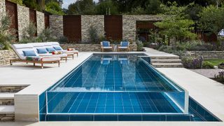 A contemporary swimming pool space over two levels with surrounding walls and sun loungers