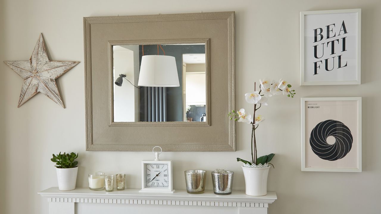 White potted orchid on white mantlepiece in living room next to candles and clock underneath mirror 