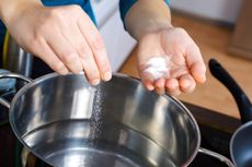 A person adds salt to water while cooking.