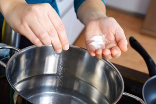A person adds salt to water while cooking.