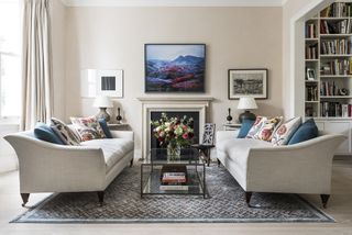 balanced living room with cream walls and two cream sofas a fireplace and artwork sit in the center