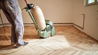 Person using a sanding machine to sand down hardwood floor panels.