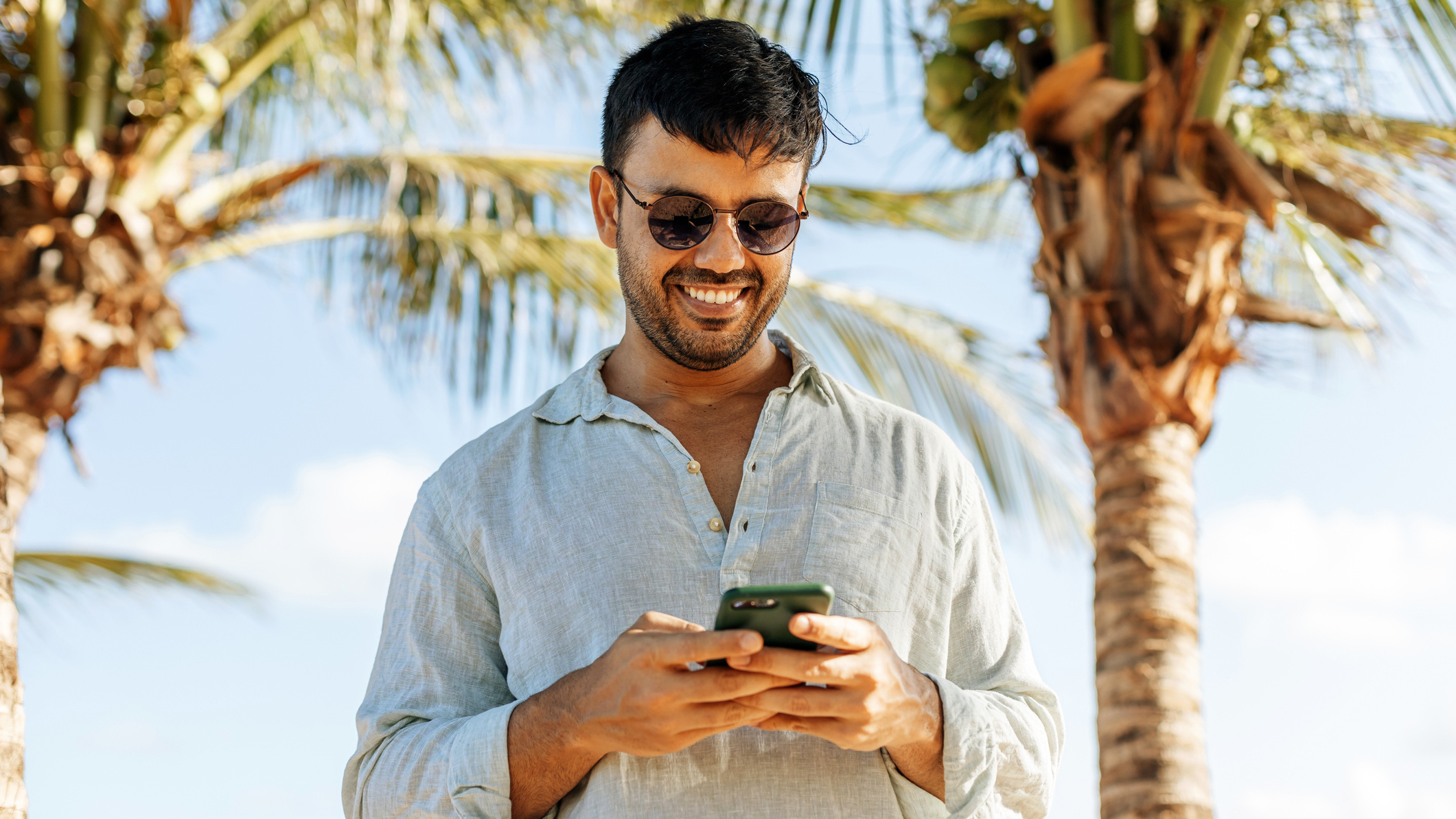Person using a smartphone on a beach, palm trees in the background