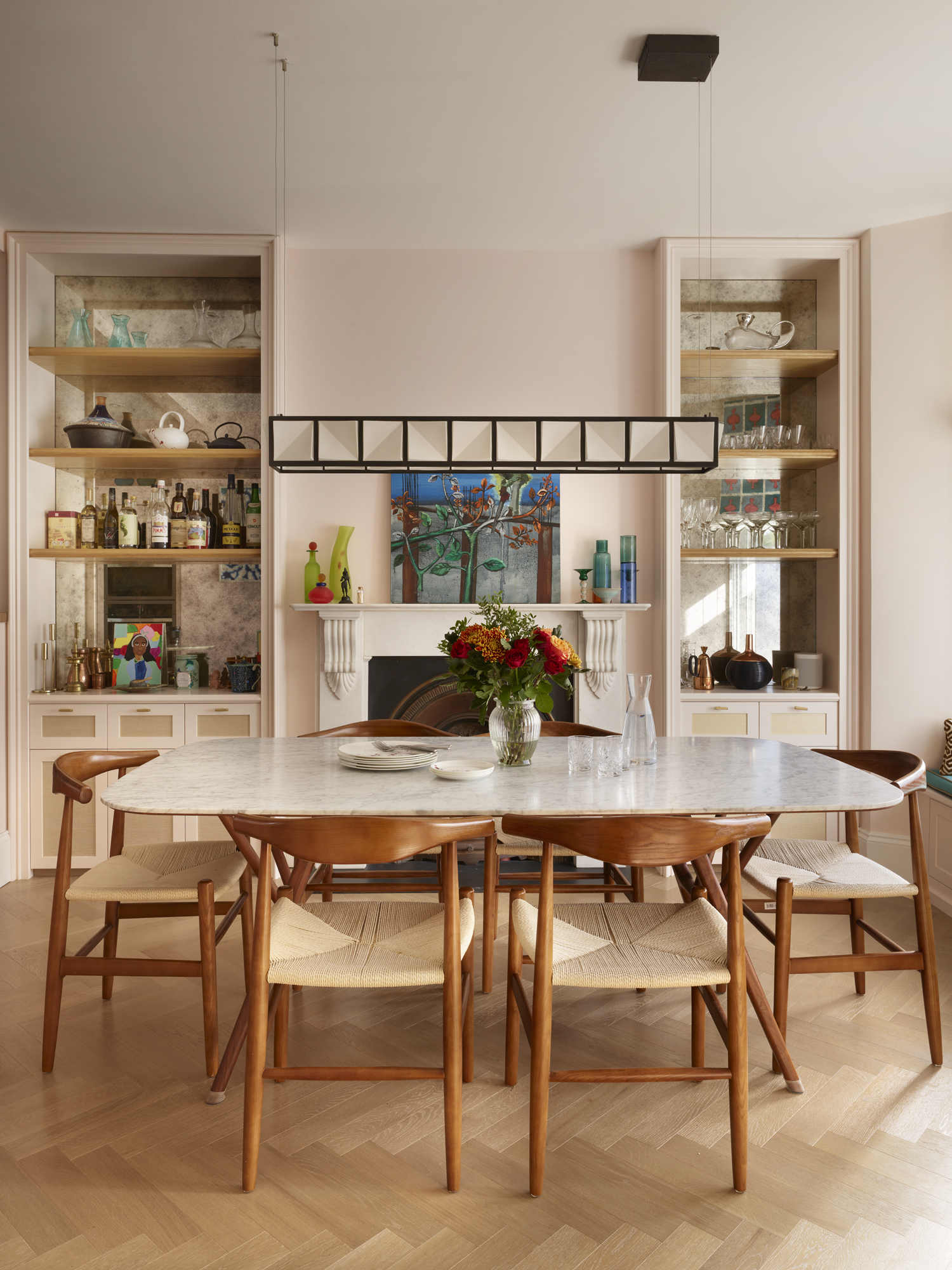 Image of a modern but traditional dining room with light pink walls and built-in shelving on either side of the fireplace. The dining table is marble with wooden chairs around it