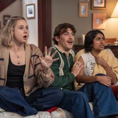 Three people (Lucy Freyer as Billie, Jack Innanen as Paul Baker, Amita Rao as Issa) look surprised while sitting on a living room couch, in 'Adults'.