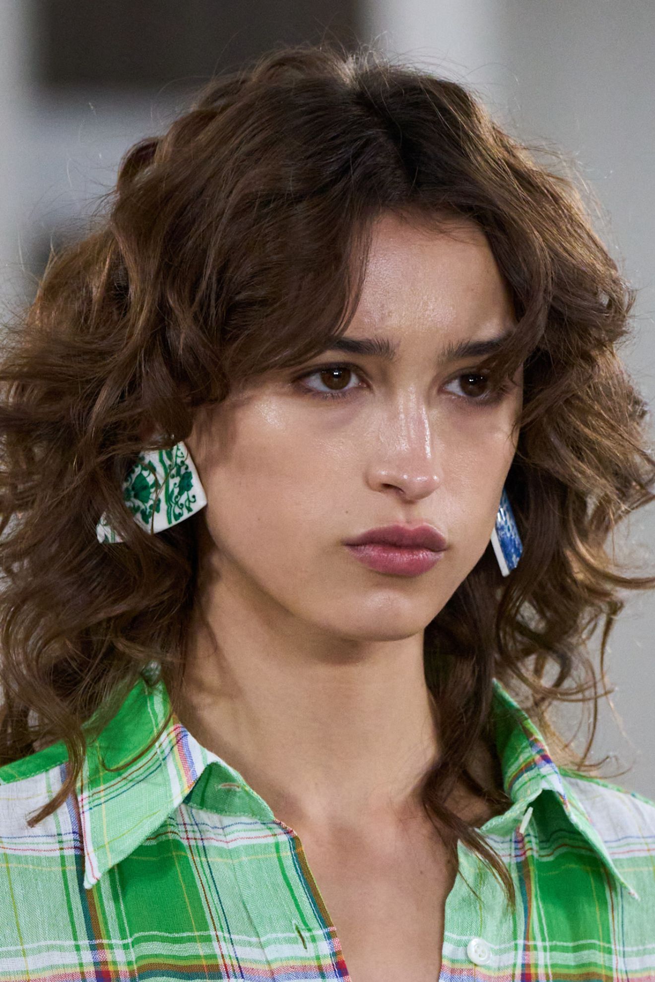 A model at the Moschino SS26 show wearing a checked shirt and statement earrings with a wavy hairstyle