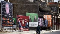 A man rides his scooter past posters and banner depicting political candidates from the rival blocs, competing for a seat in the Iraqi Council of Representatives, days before the Parliamentary elections, in Old Mosul, northern Iraq
