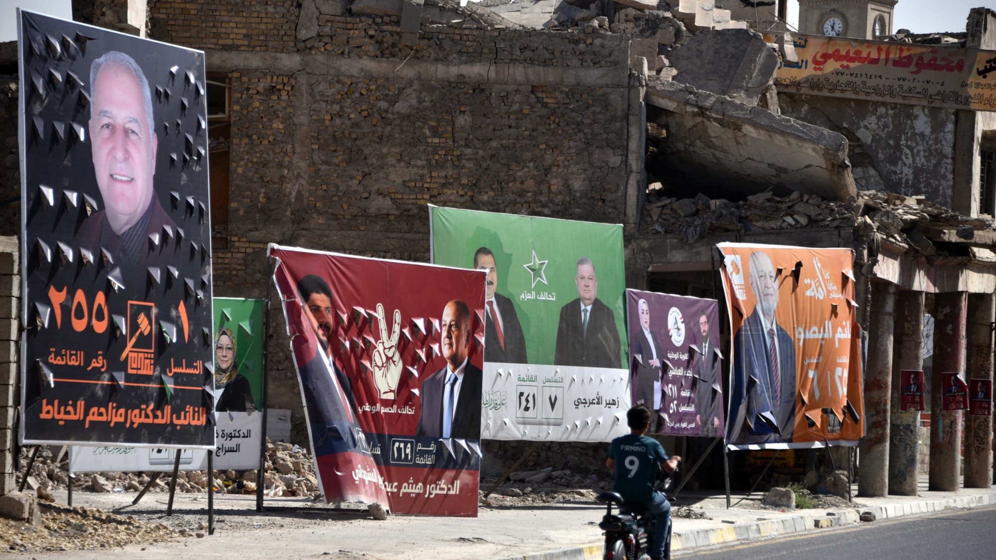 A man rides his scooter past posters and banner depicting political candidates from the rival blocs, competing for a seat in the Iraqi Council of Representatives, days before the Parliamentary elections, in Old Mosul, northern Iraq