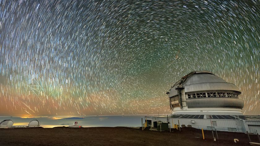In this long exposure image, a series of rings and streaks in concentric circles fill the colorful blue, orange, and green night sky with a domed roof of an observatory below. 
