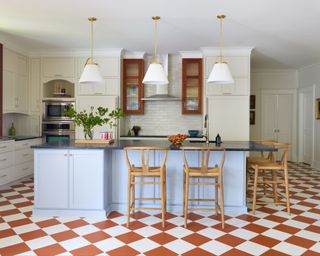 modern kitchen with red and white checked floor, light blue kitchen island, off-white walls and white and brass pendant lights